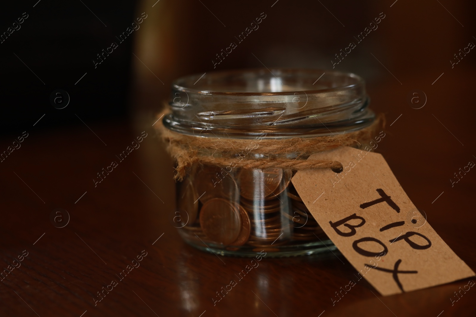 Photo of Tip box full of coins on wooden table in cafe, closeup