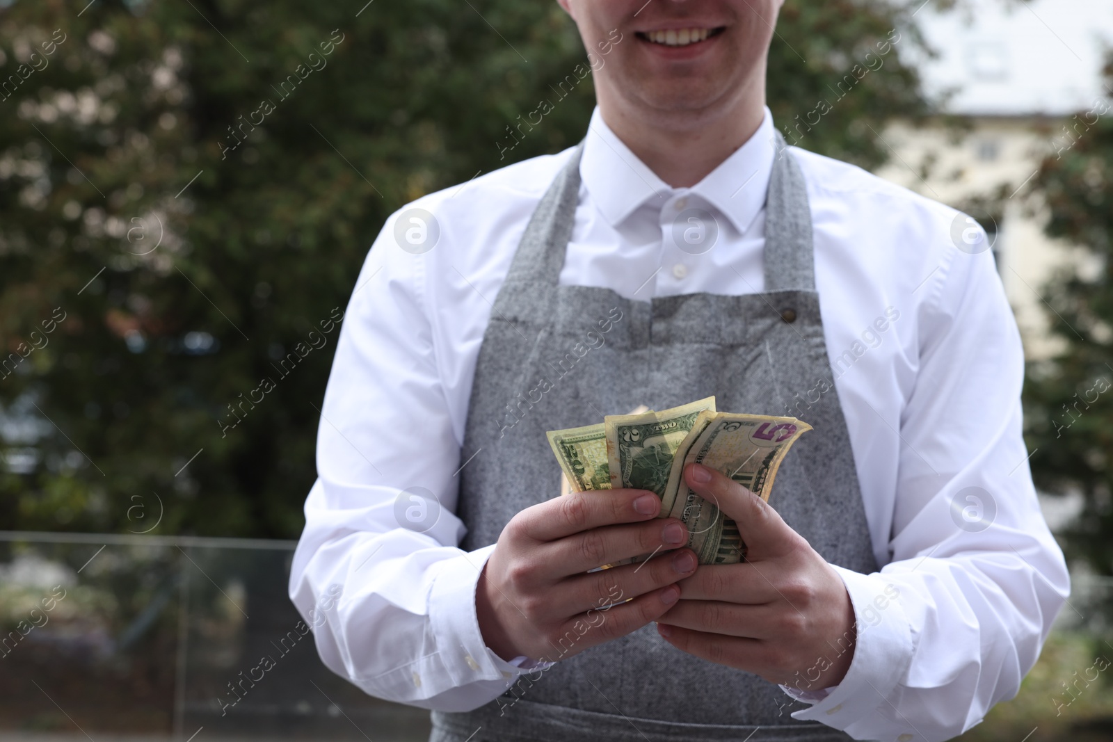 Photo of Happy waiter holding tips in outdoor cafe, closeup