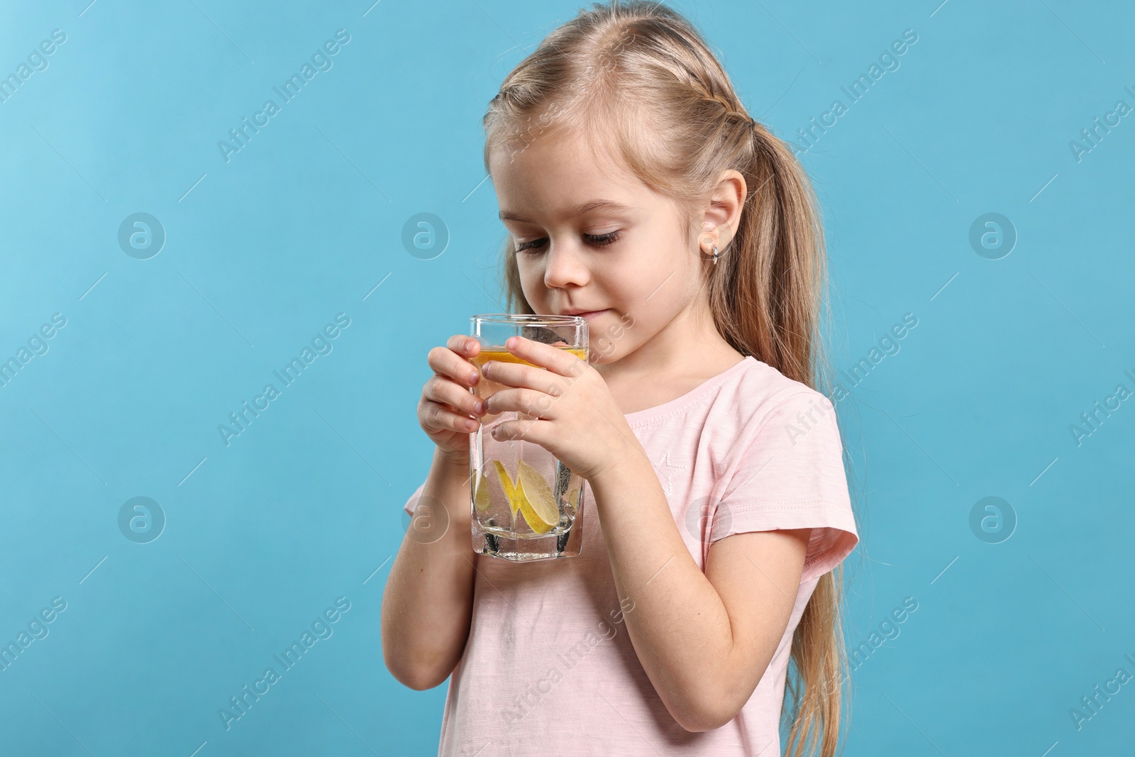 Photo of Girl with glass of lemonade on light blue background. Refreshing drink