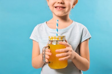 Photo of Girl with glass of orange juice on light blue background, closeup. Refreshing drink