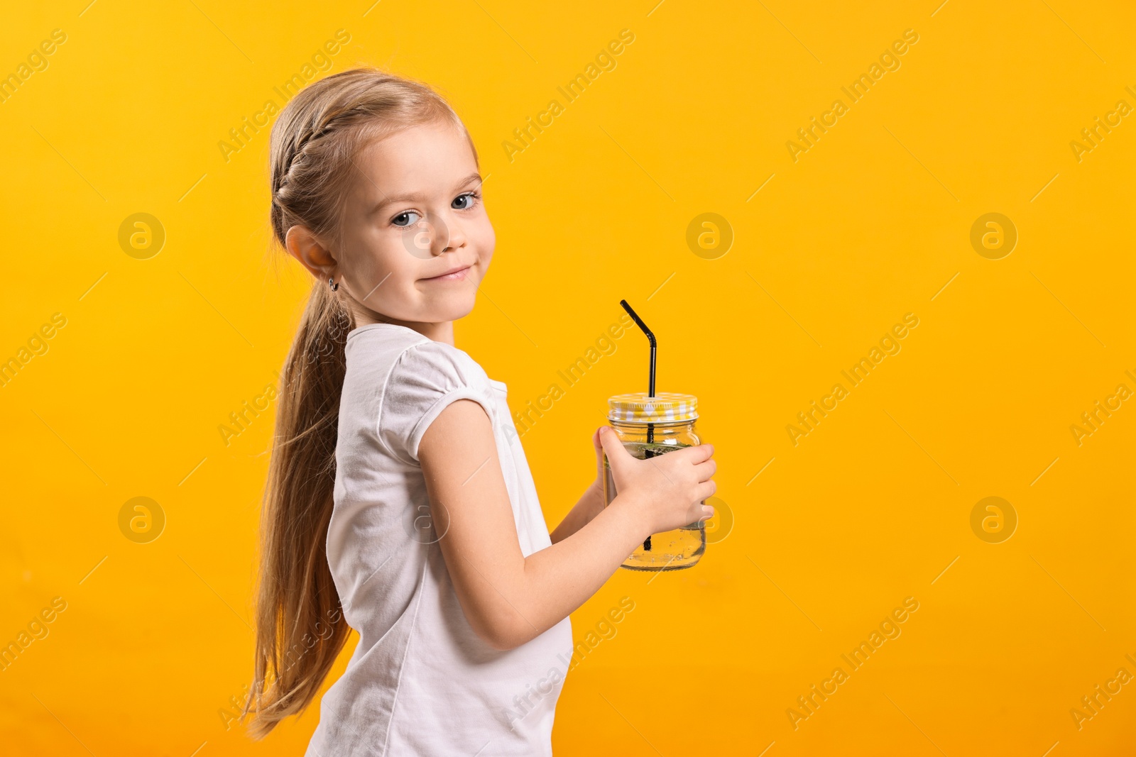 Photo of Girl with mason jar of cucumber water on orange background, space for text. Refreshing drink