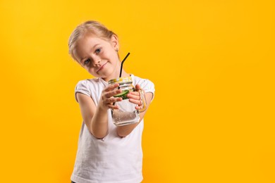 Photo of Girl with mason jar of cucumber water on orange background, space for text. Refreshing drink