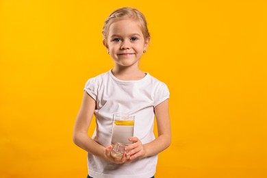 Girl with glass of lemonade on orange background. Refreshing drink