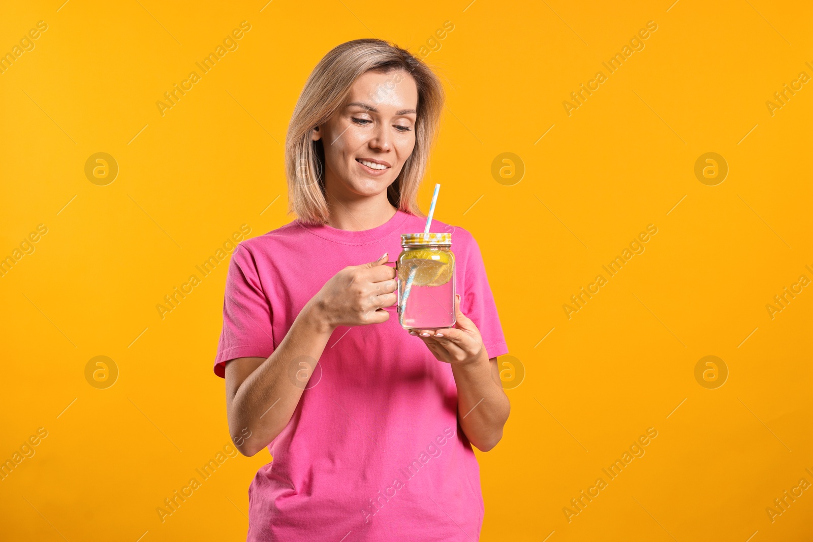 Photo of Woman with mason jar of lemonade on orange background. Refreshing drink