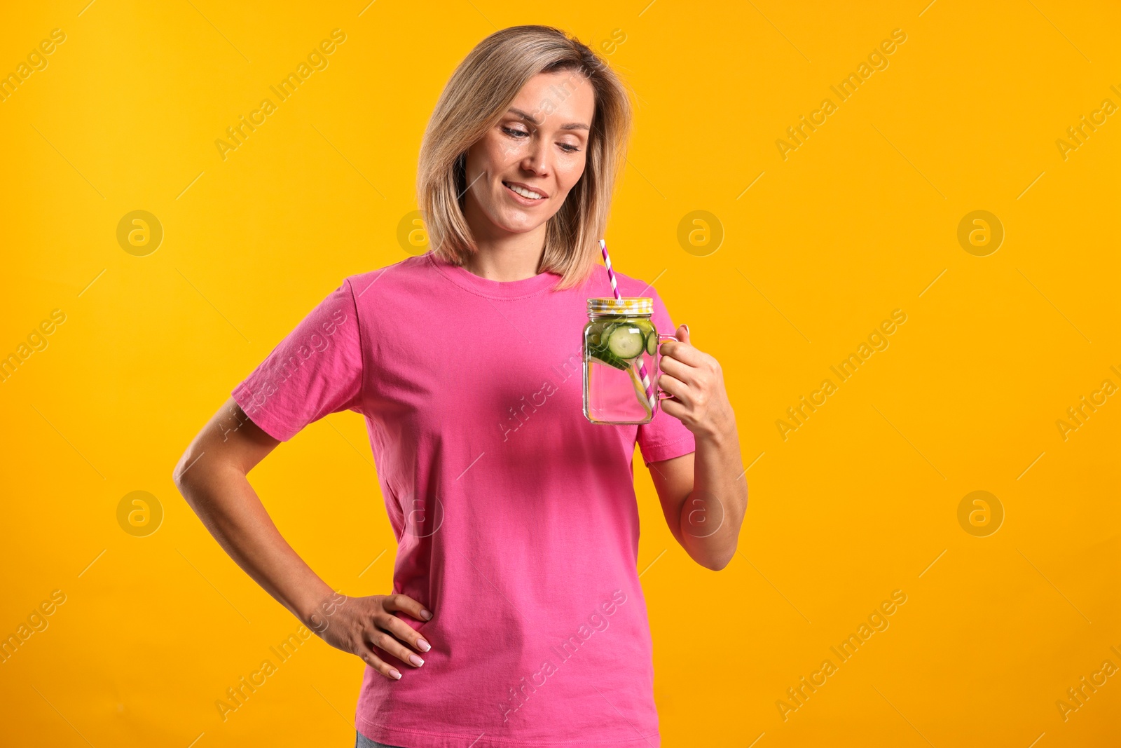 Photo of Woman with mason jar of water with cucumber on orange background. Refreshing drink