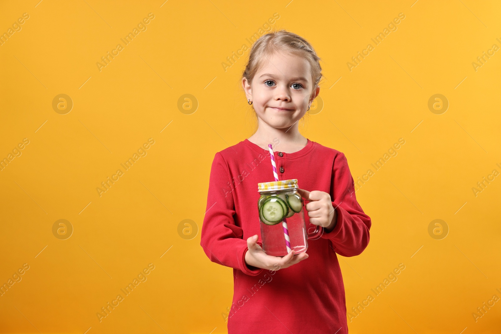 Photo of Girl with mason jar of cucumber water on orange background. Refreshing drink