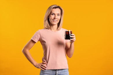 Photo of Woman with glass of refreshing soda drink on orange background.