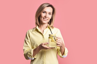 Photo of Woman with mason jar of lemonade on pink background. Refreshing drink