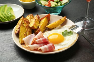 Photo of Tasty brunch. Fried egg, potato and bacon on dark textured table, closeup