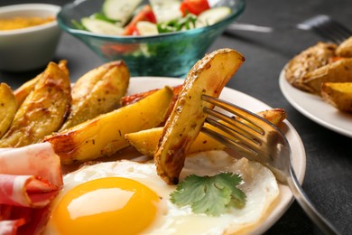 Photo of Tasty brunch. Fried egg, potato, bacon and fork on dark table, closeup