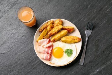 Photo of Tasty brunch. Fried egg, potato and bacon served on dark textured table, flat lay