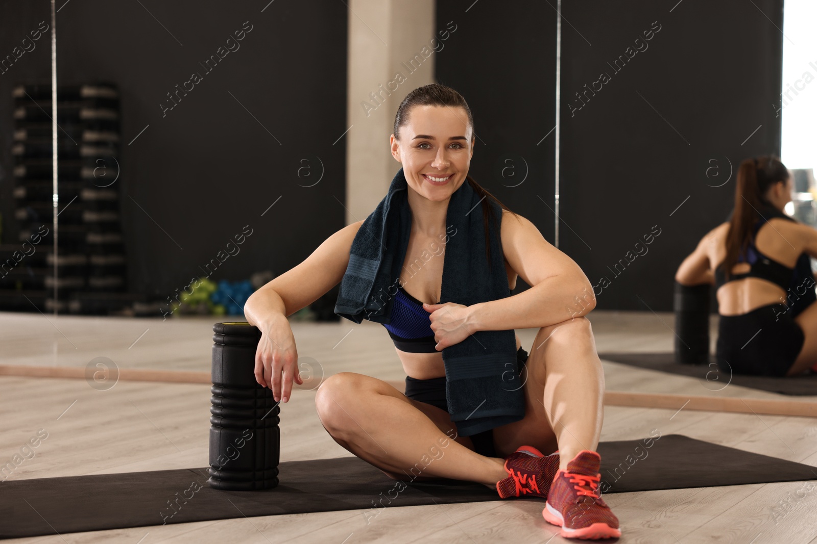 Photo of Happy woman with towel and foam roller on mat in fitness studio