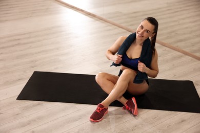 Photo of Happy woman with towel on mat in fitness studio. Space for text