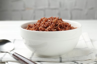 Photo of Tasty brown rice in bowl and spoon on white table, closeup