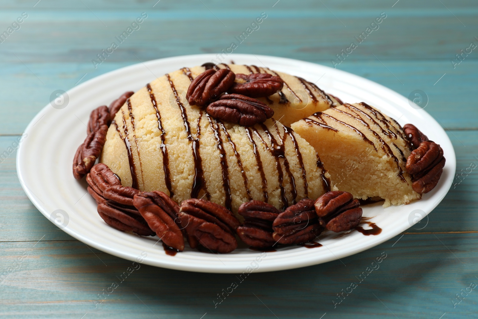 Photo of Delicious sweet semolina halva with pecans on blue wooden table, closeup