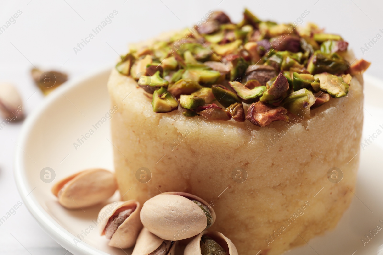 Photo of Delicious sweet semolina halva with pistachios on white table, closeup