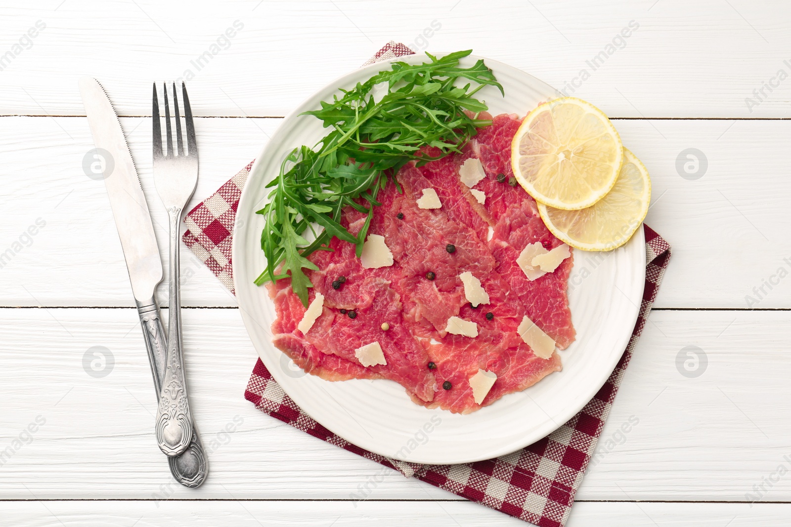 Photo of Fresh beef carpaccio with arugula, lemon and cheese served on white wooden table, flat lay