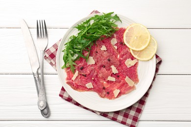 Photo of Fresh beef carpaccio with arugula, lemon and cheese served on white wooden table, flat lay