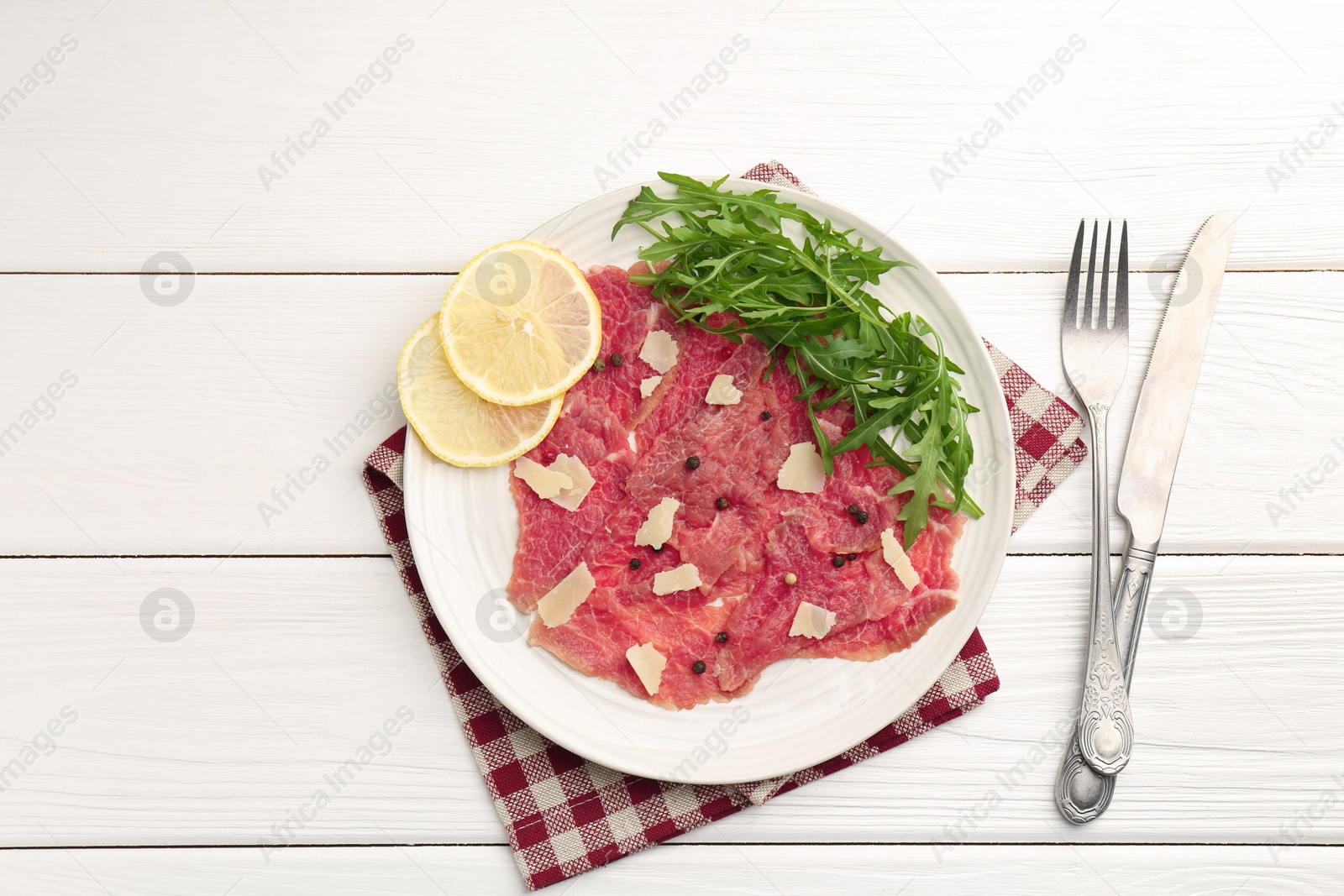 Photo of Fresh beef carpaccio with arugula, lemon and cheese served on white wooden table, flat lay