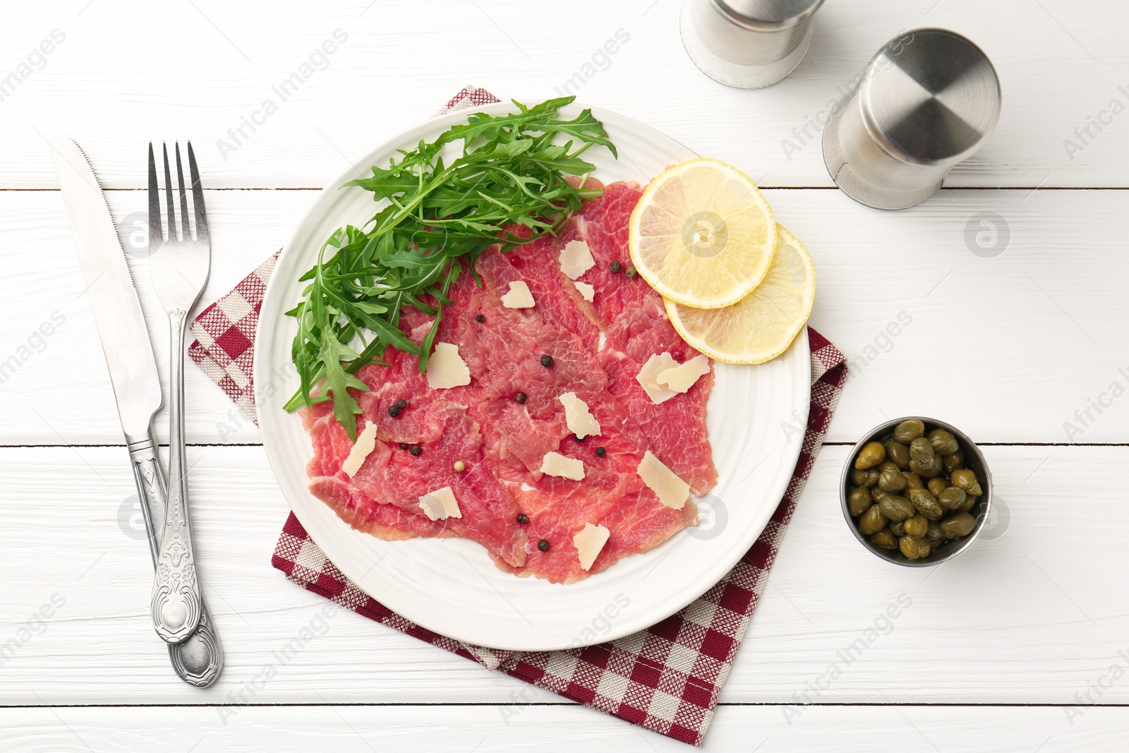 Photo of Fresh beef carpaccio with arugula, lemon and cheese served on white wooden table, flat lay