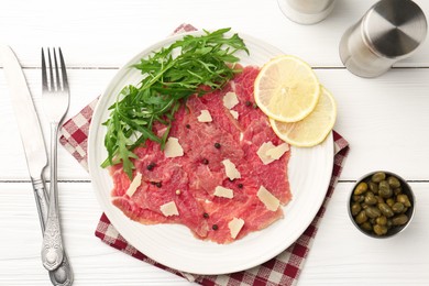 Photo of Fresh beef carpaccio with arugula, lemon and cheese served on white wooden table, flat lay