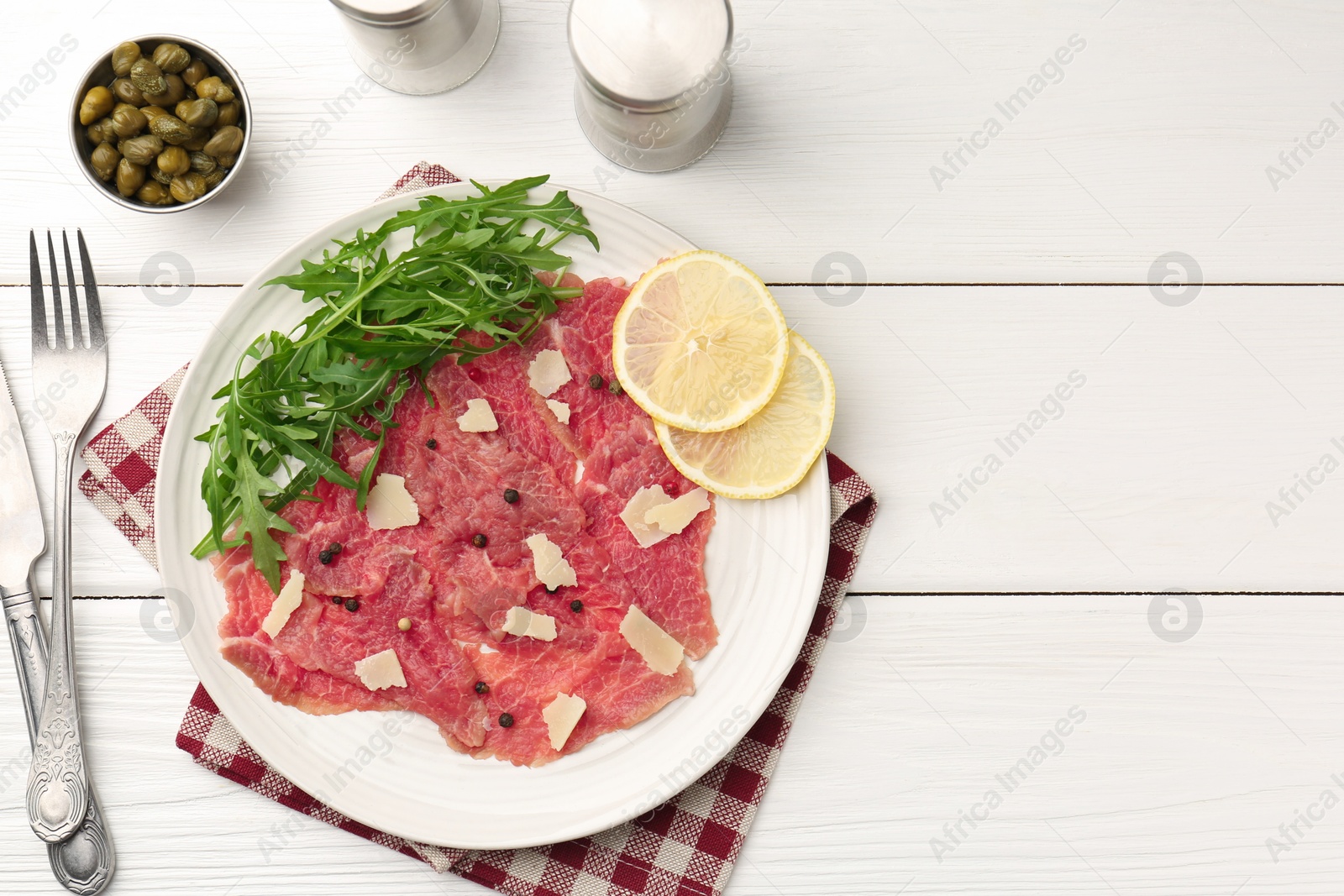 Photo of Fresh beef carpaccio with arugula, lemon and cheese served on white wooden table, flat lay. Space for text