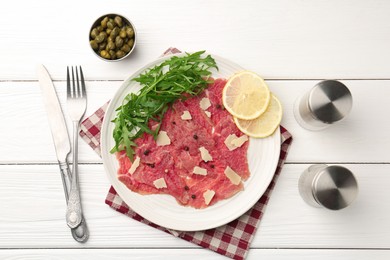 Photo of Fresh beef carpaccio with arugula, lemon and cheese served on white wooden table, flat lay