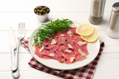 Fresh beef carpaccio with arugula, lemon and cheese on white wooden table, closeup