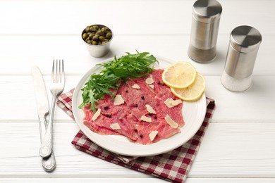 Photo of Fresh beef carpaccio with arugula, lemon and cheese on white wooden table