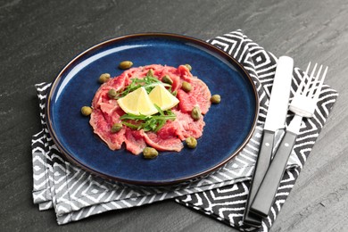 Fresh beef carpaccio with arugula, lemon and capers on dark textured table, closeup