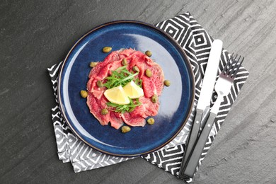 Fresh beef carpaccio with arugula, lemon and capers on dark textured table, top view