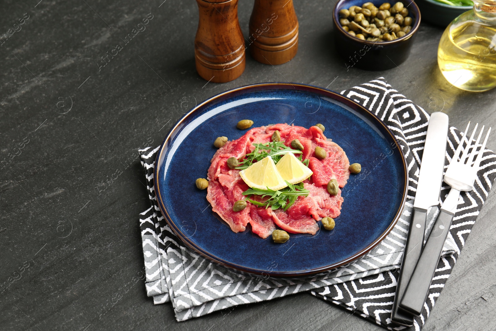 Fresh beef carpaccio with arugula, lemon and capers on dark textured table Photo of Fresh beef carpaccio with arugula, lemon and capers on dark textured table