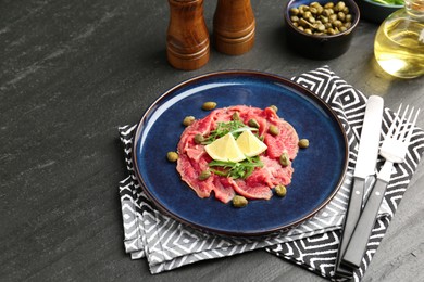 Photo of Fresh beef carpaccio with arugula, lemon and capers on dark textured table