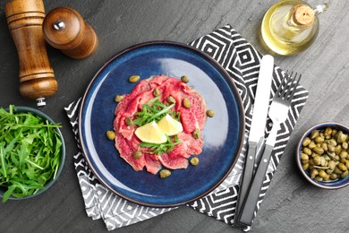 Fresh beef carpaccio with arugula, lemon and capers served on dark textured table, flat lay