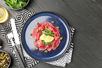 Fresh beef carpaccio with arugula, lemon and capers served on dark textured table, flat lay. Space for text