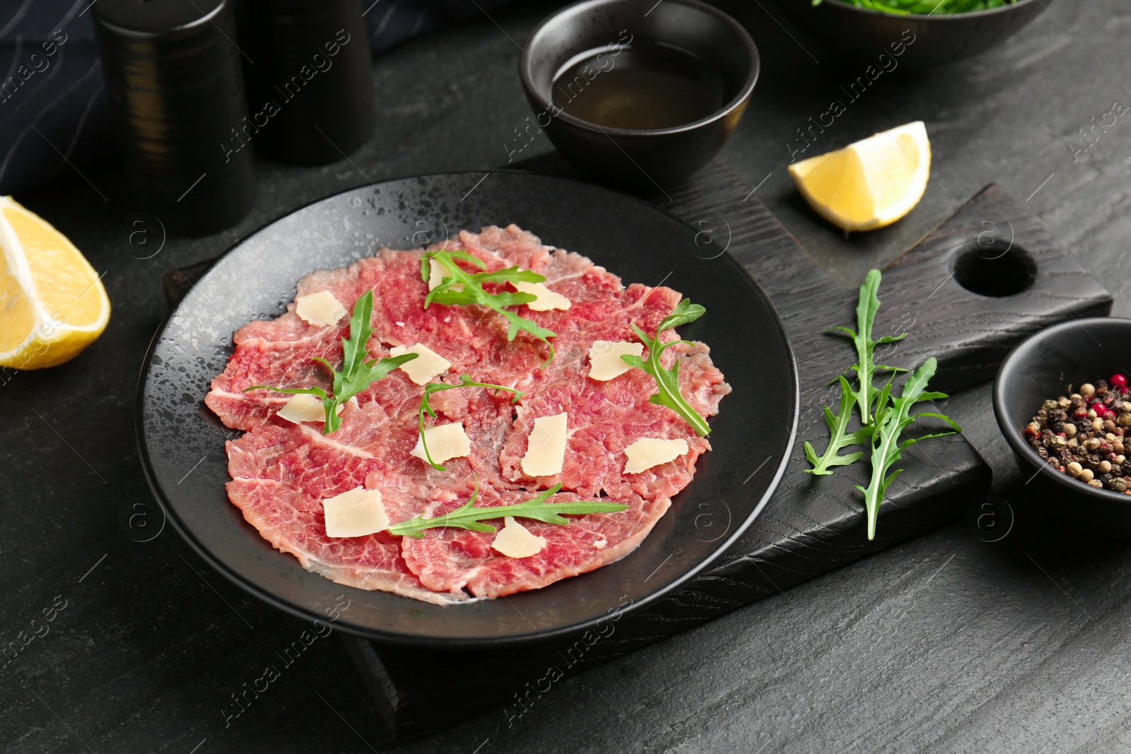 Photo of Fresh beef carpaccio with arugula and cheese on dark textured table, closeup