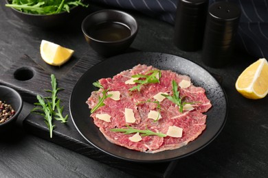 Photo of Fresh beef carpaccio with arugula and cheese on dark textured table, closeup