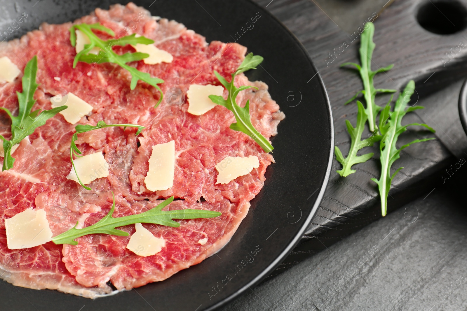 Photo of Fresh beef carpaccio with arugula and cheese on dark textured table, closeup