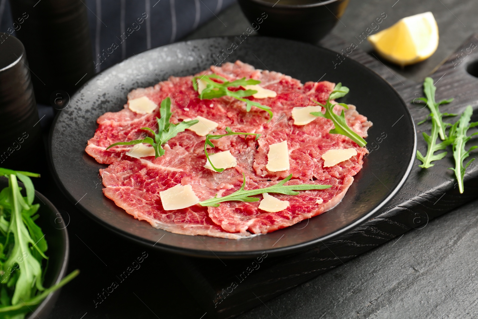 Photo of Fresh beef carpaccio with arugula and cheese on dark textured table, closeup