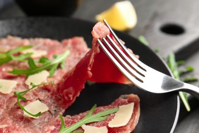 Eating fresh beef carpaccio with arugula and cheese on dark table, closeup