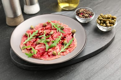 Fresh beef carpaccio with arugula, capers and sauce on dark textured table