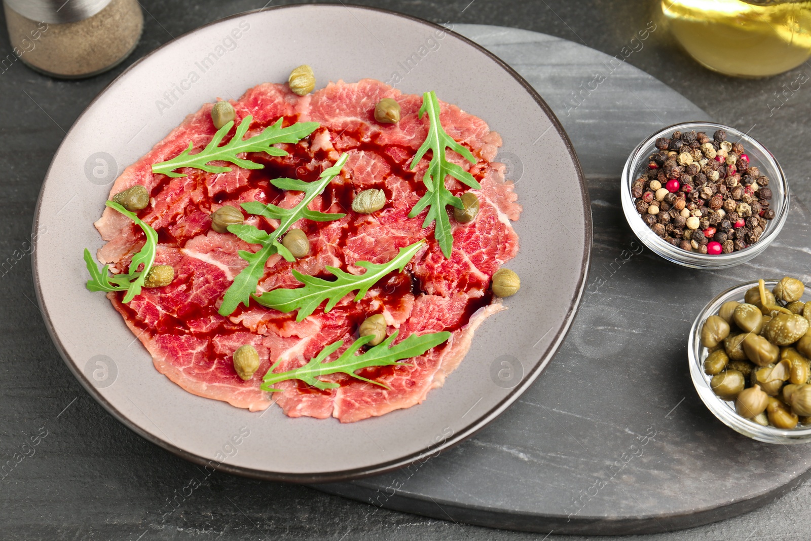 Photo of Fresh beef carpaccio with arugula, capers and sauce on dark textured table, above view