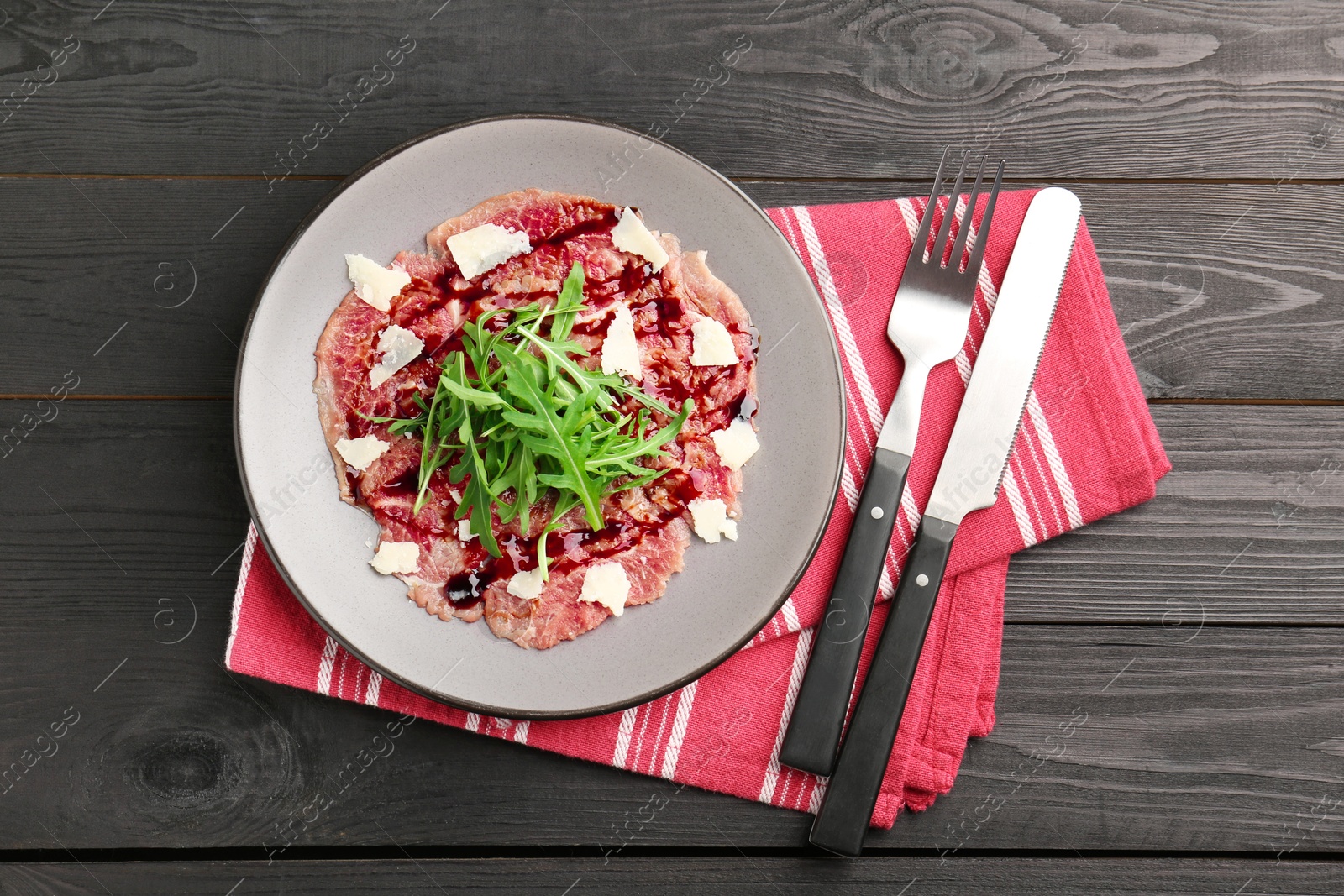 Photo of Fresh beef carpaccio with arugula, cheese and sauce on black wooden table, top view