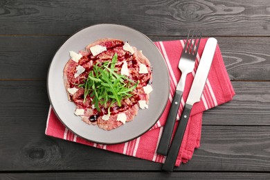 Photo of Fresh beef carpaccio with arugula, cheese and sauce on black wooden table, top view