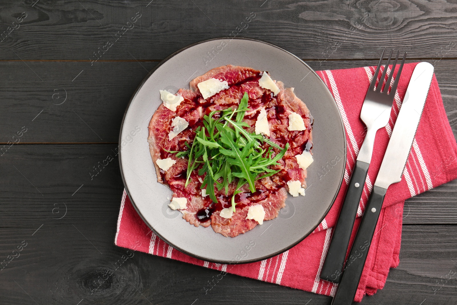 Photo of Fresh beef carpaccio with arugula, cheese and sauce on black wooden table, top view