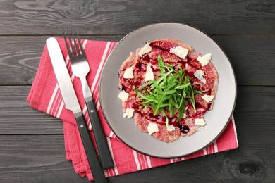 Photo of Fresh beef carpaccio with arugula, cheese and sauce on black wooden table, top view