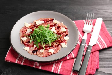 Fresh beef carpaccio with arugula, cheese and sauce on black wooden table, closeup