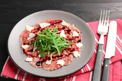 Photo of Fresh beef carpaccio with arugula, cheese and sauce on black wooden table, closeup