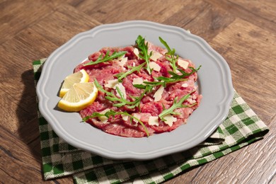 Photo of Fresh beef carpaccio with arugula, cheese and lemon on wooden table, closeup