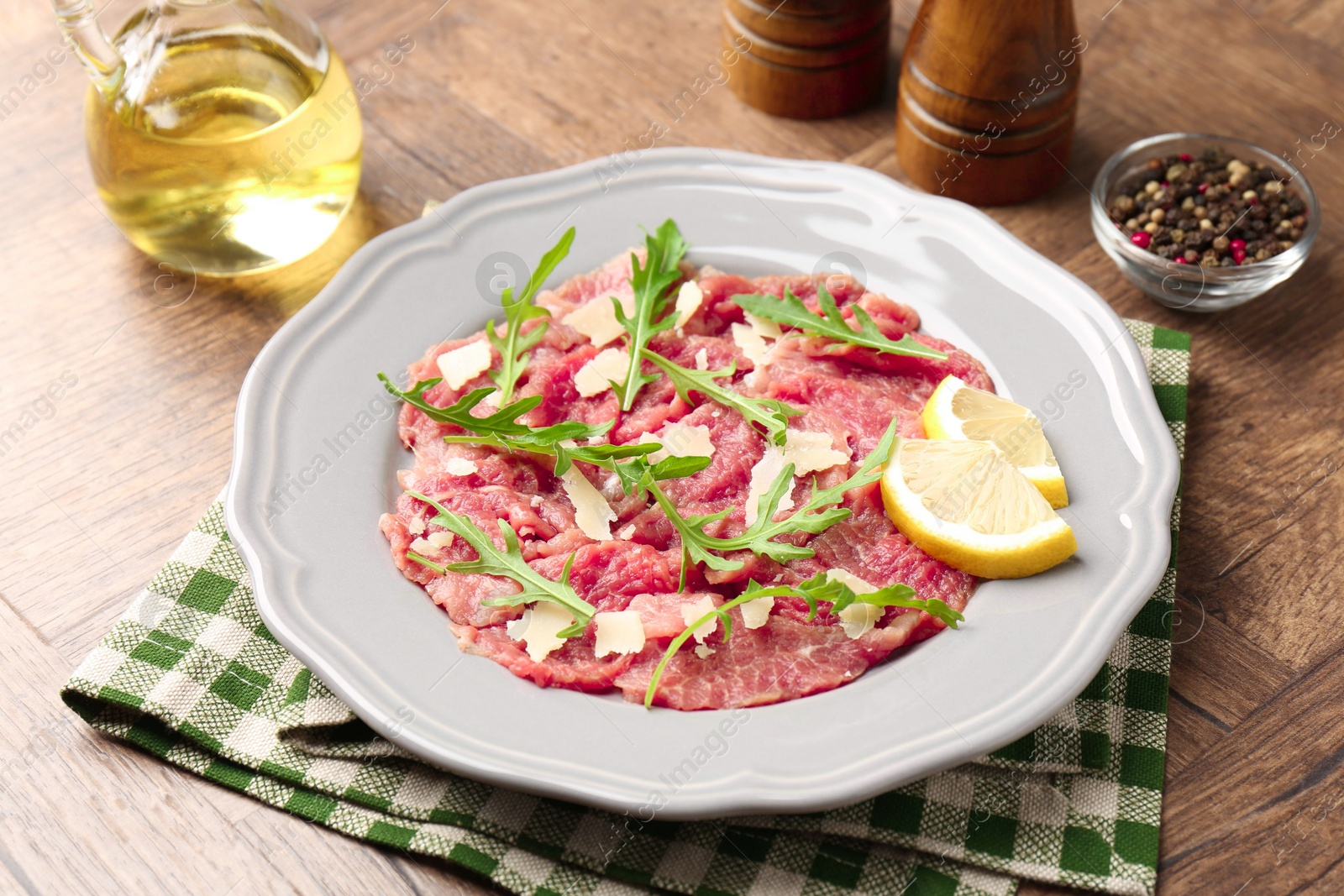 Photo of Fresh beef carpaccio with arugula, cheese and lemon on wooden table, closeup